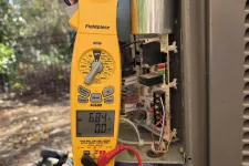 Thumbnail for Residential AC Heat Repair in Marietta 30068 by The Air Company of GA.  Yellow Fieldpiece clamp meter measuring current on HVAC unit wiring outdoors with capacitor in background.