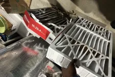Thumbnail for Person holding a new white 16x25x4 air filter next to a used dirty filter in a basement or storage area.