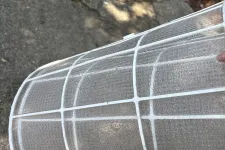 Thumbnail for Close-up of a white plastic air conditioner filter with mesh grid held outdoors on a concrete surface.