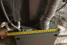 Thumbnail for Measuring the width of a furnace unit with a tape measure showing 22 inches in a basement duct setup.