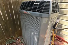 Thumbnail for Outdoor HVAC unit installed next to house siding and wooden fence surrounded by mulch and plants.