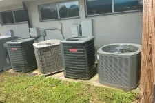 Thumbnail for Four outdoor air conditioning units lined up outside a residential building on a sunny day.