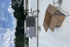 Thumbnail for Open cardboard box and rooftop HVAC unit on a flat white roof under partly cloudy sky.
