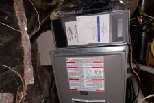 Thumbnail for Residential AC Cooling Repair in Atlanta 30318 by The Air Company.  Furnace unit installed on concrete blocks in a basement crawl space with exposed pipes and insulation.