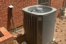 Thumbnail for Outdoor air conditioning unit installed next to brick house with tools and pinecones nearby on ground.