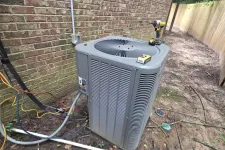 Thumbnail for Outdoor air conditioning unit installed next to a brick wall with tools and wiring around it in a backyard.