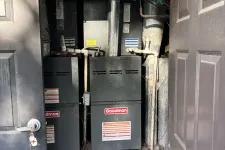 Thumbnail for Two Goodman HVAC units installed in a utility closet with open double doors and exposed pipes.