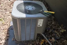Thumbnail for Outdoor air conditioning unit on a concrete pad with tools and cables, surrounded by dry leaves near a house wall.