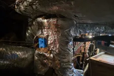Thumbnail for Foil-insulated HVAC duct with exposed blue control box and surrounding wires in a dimly lit basement.