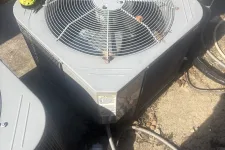 Thumbnail for Outdoor HVAC unit with protective grill and power drill on top, placed beside another air conditioning unit.