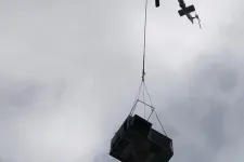 Thumbnail for Helicopter lifting a large metal container high against a cloudy sky during aerial transport.