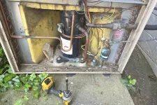 Thumbnail for Open HVAC unit showing compressor, copper pipes, wiring, insulation, and a yellow power drill on the ground.
