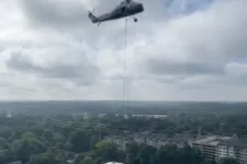 Thumbnail for Military helicopter flying above urban area with cloudy sky and buildings in the background.
