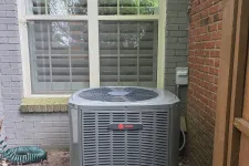 Thumbnail for Outdoor air conditioning unit installed below a double window between brick and wooden walls with garden hose nearby
