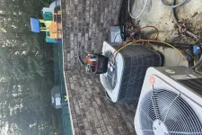 Thumbnail for Two outdoor air conditioning units with diagnostic tools attached against a brick wall in a backyard.
