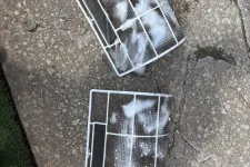 Thumbnail for Two rectangular air conditioner filters with soap suds resting on cracked concrete pavement next to grass.