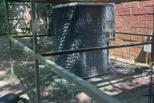 Thumbnail for Outdoor air conditioning unit protected by a metal cage beside a brick wall with tools on the ground