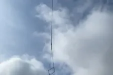 Thumbnail for Helicopter lifts a large metal frame against a cloudy sky during daytime operation.