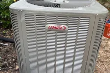 Thumbnail for Outdoor Lennox air conditioning unit installed on a black plastic base surrounded by greenery and mulch.
