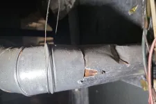 Thumbnail for Rusty and cracked metal duct pipe in a dimly lit attic with insulation and wiring nearby.