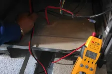 Thumbnail for HVAC Repair, Maintenance and Installation in Roswell by The Air Company of GA. Technician using a yellow digital multimeter to test electrical wiring inside a panel with multicolored cables.