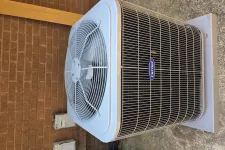 Thumbnail for Outdoor Carrier air conditioning unit with protective metal grilles on concrete pad by brick wall