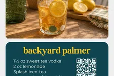 Thumbnail for Glass of iced Backyard Palmer cocktail with lemon wheel on wooden table and fresh lemons in background.