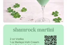 Thumbnail for Green shamrock martini with whipped cream and chocolate shavings in a martini glass with shamrocks on white surface.