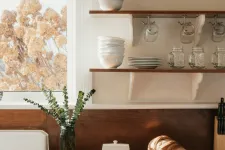 Thumbnail for Cozy kitchen corner with wooden countertop, stacked white dishes, glass jars, copper kettle, and sliced bread under sunlight