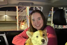 Thumbnail for Smiling woman in car holding a corgi dog with a pink tag, phone, and night street lights in background