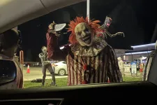 Thumbnail for Scary clown with red hair and striped costume holding a cleaver outside a car at night during Halloween event.