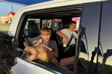 Thumbnail for Two boys sitting inside a car with two French bulldogs looking out the open window during dusk.