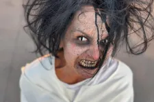 Thumbnail for Person with wild black hair and scary makeup wearing a white straitjacket looking up fiercely.