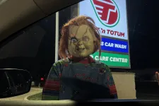 Thumbnail for Chucky doll with red hair and overalls standing outside a car window at night near a gas station sign.