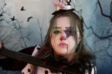 Thumbnail for Person dressed as a creepy clown with polka dot and striped outfit, smeared makeup, holding blood-stained sword