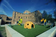 Thumbnail for a large building with a lawn and a playground in front of it