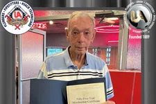 Thumbnail for Senior man holding a 55-year membership certificate with logos of plumbers and pipefitters union in background.