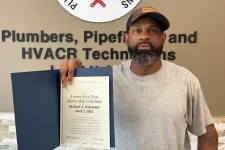 Thumbnail for Man holding a certificate standing next to Plumbers and Pipefitters union sign on wall