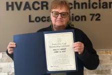 Thumbnail for Person holding a certificate standing next to a Plumbers and Pipefitters Union Local 72 sign on a beige wall.
