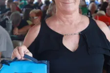 Thumbnail for Woman holding a blue YETI cooler bag and event tickets at an outdoor gathering under a tent.