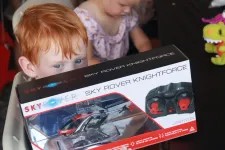 Thumbnail for Young red-haired child holding a Sky Rover Knightforce remote control helicopter box with another child in background.