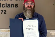 Thumbnail for Bearded man in red hat holding certificate standing next to Plumbers, Pipefitters & HVACR Technicians Local Union 72 logo.