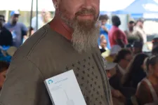 Thumbnail for Man with a beard and sunglasses holding a white product box in a crowded event tent
