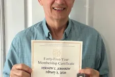 Thumbnail for Man wearing glasses and blue shirt holding a forty-five year membership certificate and a pin, smiling at the camera.