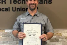 Thumbnail for Man in uniform holding certificate standing by Plumbers and Pipefitters Local Union 72 sign on wall.