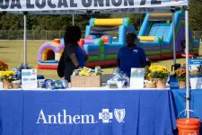 Thumbnail for Two women at an Anthem booth with snacks and flowers in front of a blue inflatable play area outdoors