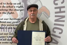 Thumbnail for Man holding a thirty-year membership certificate standing in front of a wall with union text and graphics.