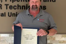 Thumbnail for Man proudly holding certificate standing by Plumbers, Pipefitters & Service Technicians union sign on wall