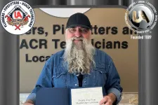 Thumbnail for Man with long beard holding a 25-year membership certificate for plumbers and pipefitters union.