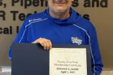 Thumbnail for Man in blue jacket holding certificate in front of Plumbers and Pipefitters Union Local 72 logo and wall text